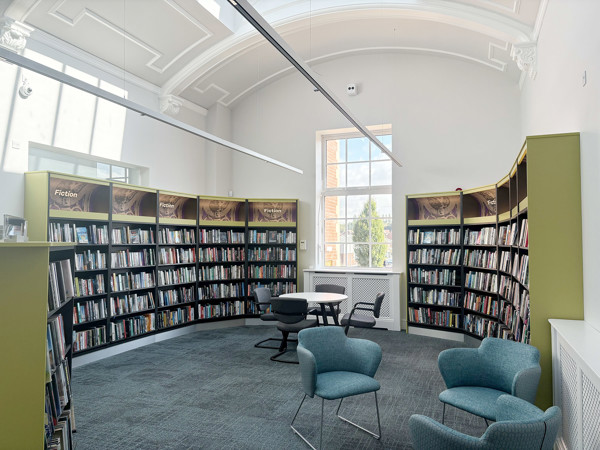 Curved shelving units filled with fiction titles beside a round table and chairs in a quiet reading space at Royton Library