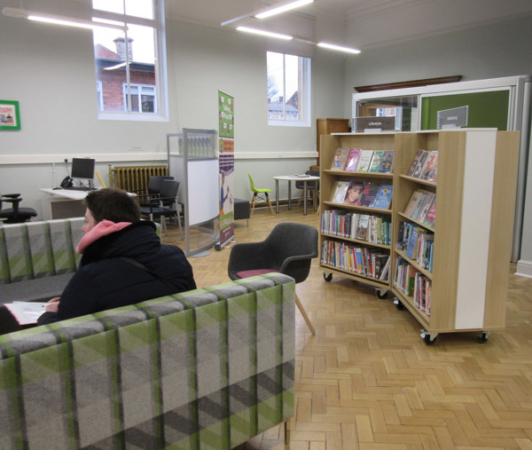 Grey and green upholstered seating beside a mobile browsing shelf in a public library browsing area at Morley Library