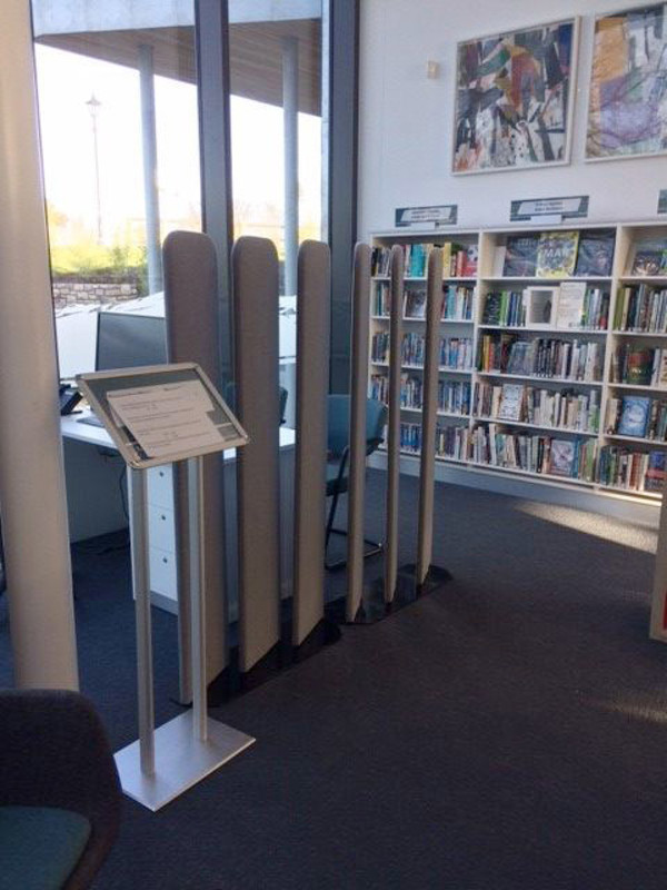Slim, grey information stands beside a computer station in a public library browsing area at Conwy Culture Centre
