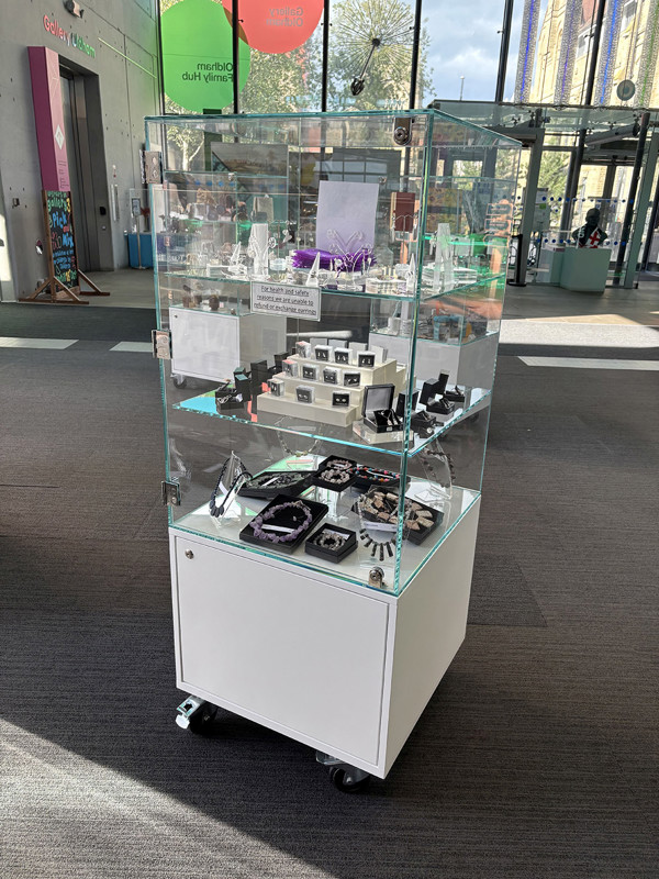 Glass display case showcasing various jewellery pieces on a mobile unit in the retail area at Oldham Library & Gallery Shop – jewellery