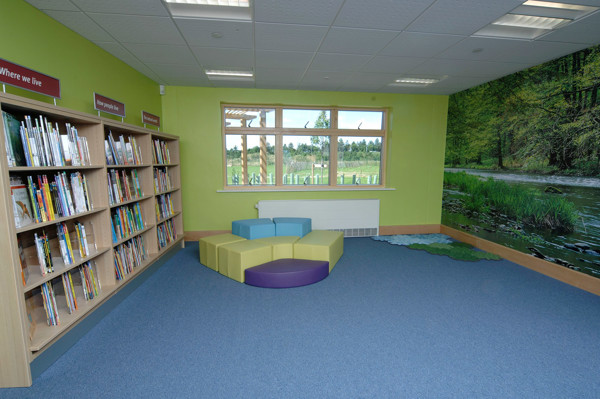Colourful seating area with a circular soft seating unit beside browsing shelves at Orchard Park Primary School