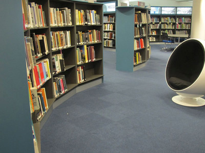 Curved grey shelving units filled with books beside a circular white lounge chair in an open-plan library space at Boots Library