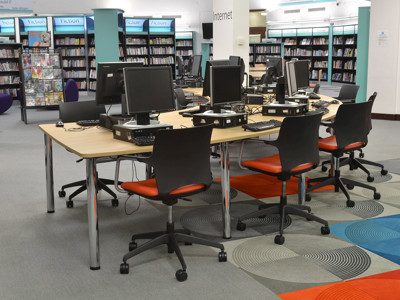 Black office chairs with orange seat cushions around a collaborative work table in a public library browsing area at Fullwell Cross Library
