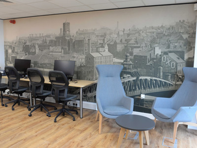 Two grey upholstered lounge chairs and a side table beside computer workstations in a local studies area at Gateshead Archive