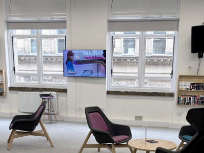 Stylish lounge chairs and a wall-mounted screen in a digital engagement area at Leeds Music Library