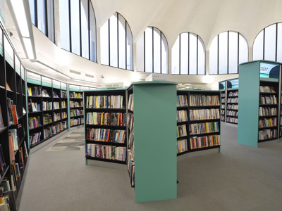 Curved black shelving units filled with books and large windows creating a light-filled browsing area at Fullwell Cross Library