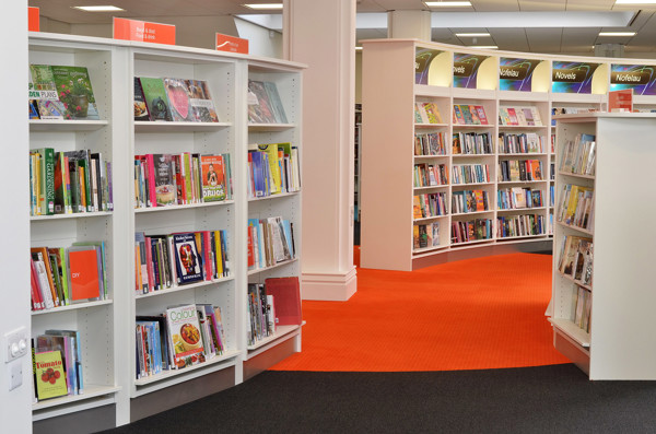 Curved browsing shelves filled with colourful book covers and an orange carpet at Llandudno Library