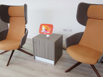 Orange upholstered lounge chairs beside a small side table with a digital display at Stafford Library