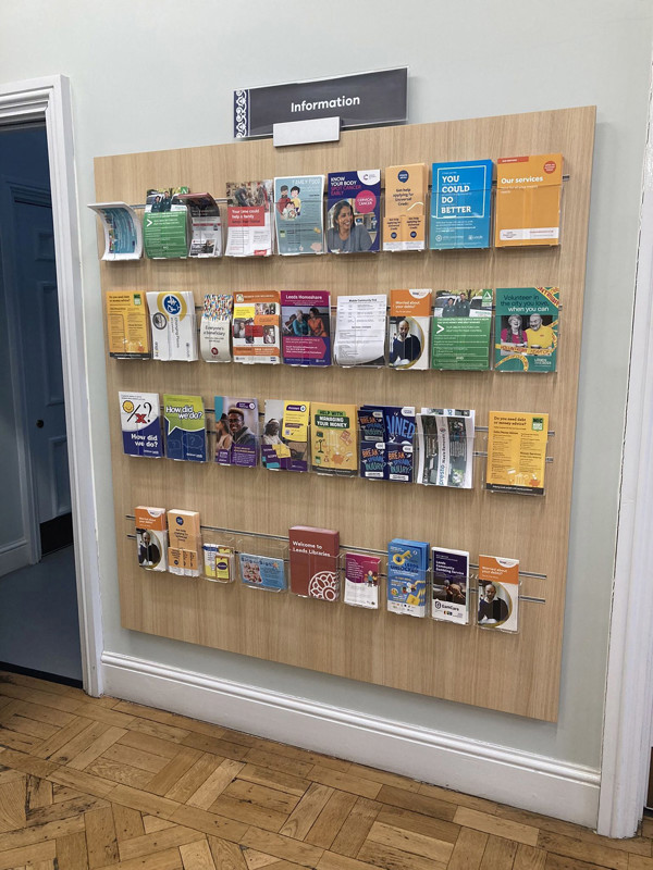 Wooden leaflet display board showcasing various informational brochures and flyers at Morley Library