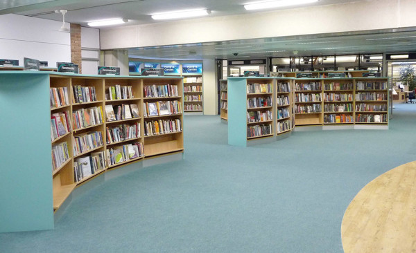 Curved wooden browsing shelves filled with books in a public library browsing area at County Library Oxfordshire