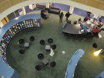 Curved blue shelving with book displays and black chairs in a study area at Boots Library