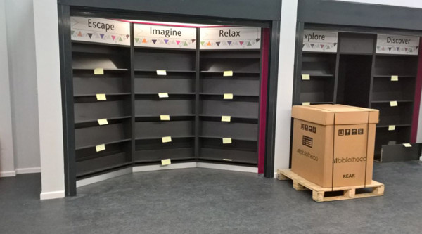 Curved shelving units with themed labels and post-it notes in a library browsing area at Barton Library