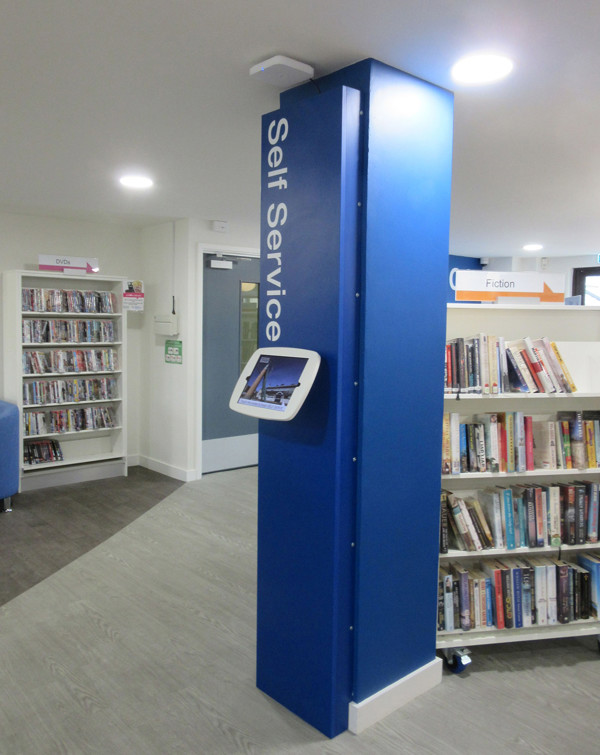 Blue self-service kiosk beside browsing shelves in the public library browsing area at Midsomer Norton Library