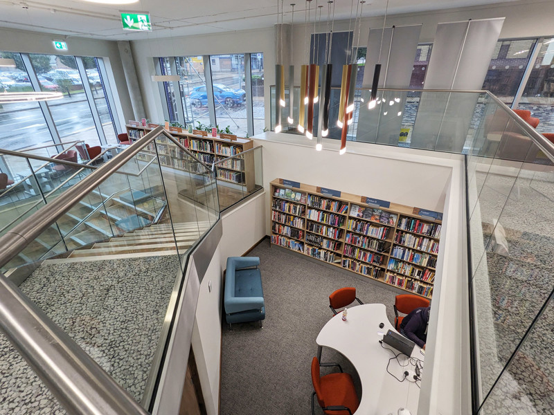 Curved shelving filled with books beside a study area featuring a round table and orange chairs at City Central Library Stoke On Trent