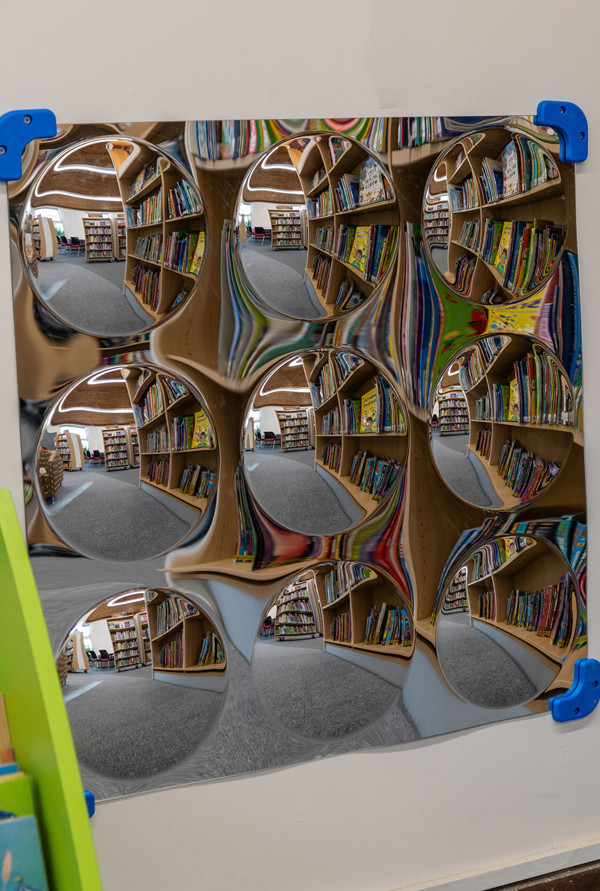 Reflective circular mirrors mounted on a wall beside colourful book displays in a children's reading area at Chinnor Library