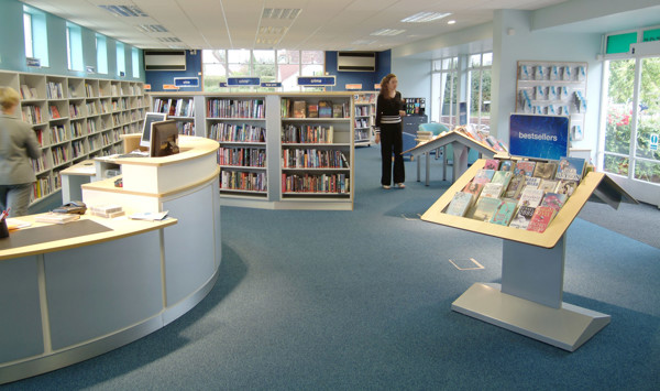 Curved circulation desk and face-out book displays in a bright browsing area at Ash Library