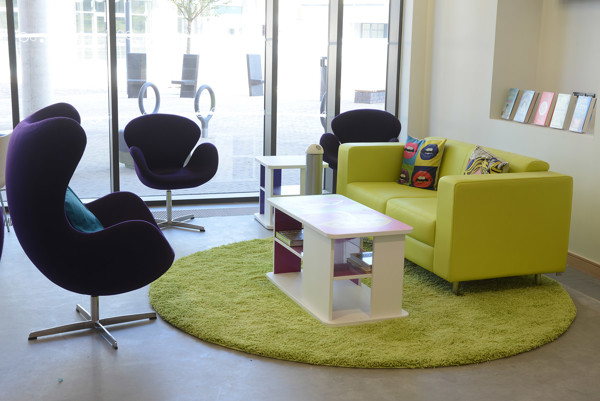Purple lounge chairs and a lime green sofa on a circular rug in a relaxed seating area at Southwater Library