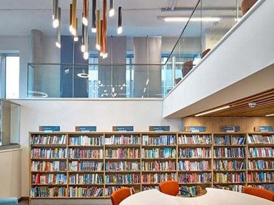 Curved white study tables and orange upholstered chairs beside colourful book shelving at Stoke City Central Library