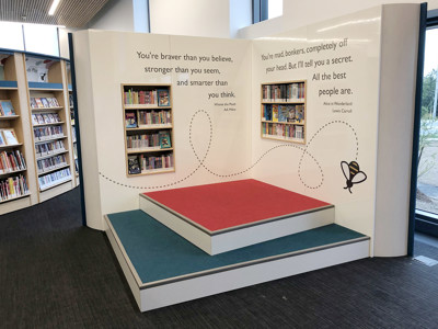 Red and blue tiered seating with book displays and inspirational quotes in a children's reading area at Sherwood Library