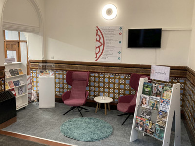 Two pink upholstered lounge chairs and a small side table beside a magazine display at BIPC Leeds