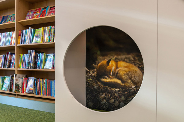 Circular cutout featuring a sleeping fox beside colourful browsing shelves filled with children's books at Chinnor Library