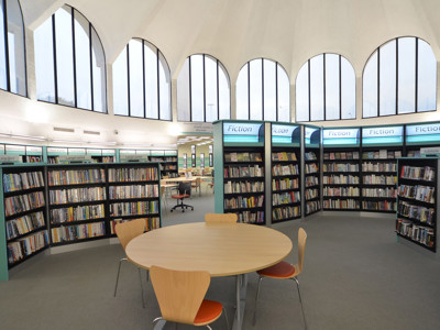 Curved bookshelves filled with fiction titles surrounding a circular study table and chairs at Fullwell Cross Library
