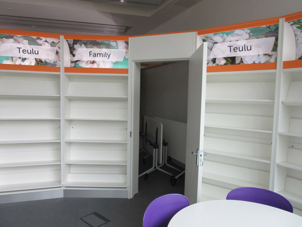 Curved shelving units with labels for "Teulu" and "Family" in a library reading area at Brecon Library