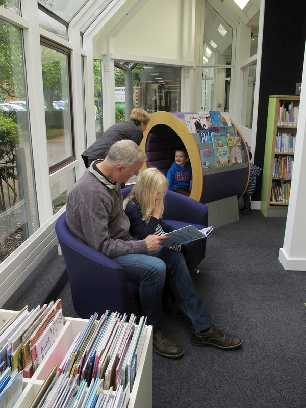 Two upholstered chairs in a children's reading area with a playful book display and a reading tunnel at Newark Library