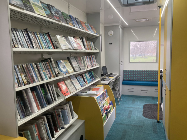 Face-out book displays and a computer workstation beside a blue upholstered bench at Leeds Mobile Community Hub