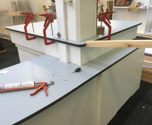 Clamps securing a countertop edge with tools and materials on a work surface at South Woodford Library