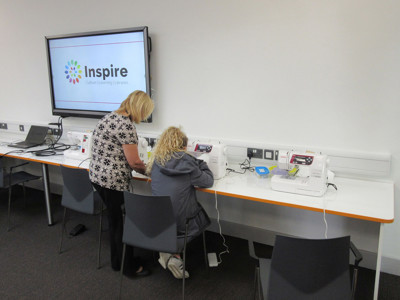 Two individuals using sewing machines at a long work table in a makerspace at Beeston Library