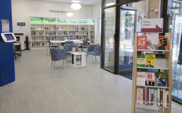 Blue patterned lounge chairs and a white coffee table in a reading area with browsing shelves at Midsomer Norton Library