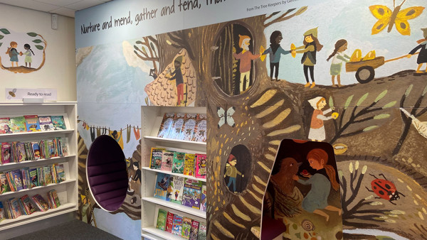 Colourful mural depicting children interacting with nature alongside a book display at Blaydon Library
