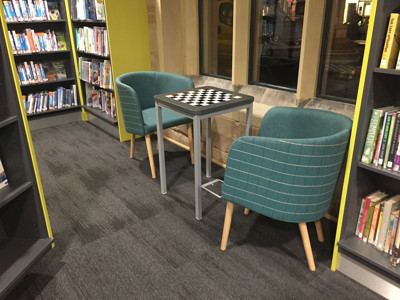 Two teal upholstered chairs and a small chess table in a quiet reading space at Lichfield Library