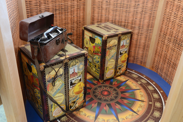 Decorative storage trunks with travel-themed designs and a vintage suitcase on a patterned circular floor at Southwater Library