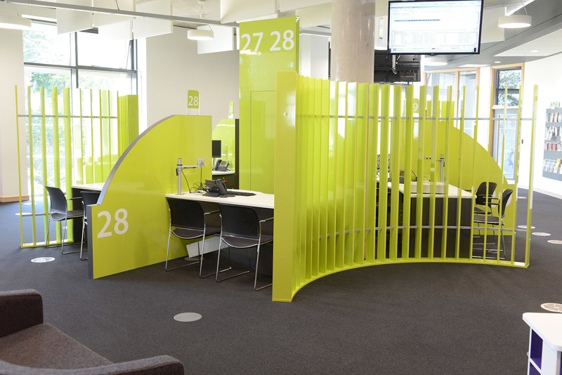 Bright green partitioned service desks with black chairs in a public library advice area at Southwater Customer Services