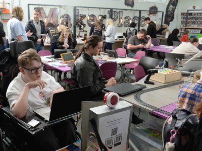Participants engaged in various activities at collaborative work tables in the open-plan makerspace at Gateshead Makerplace