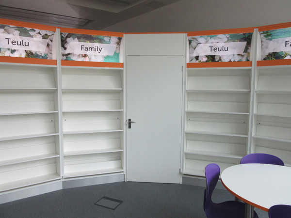 Curved shelving units with empty book displays and signage in a family reading area at Brecon Library
