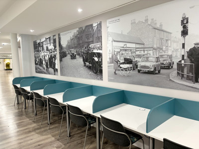 Light blue study booths with white tables and grey chairs beside historical black-and-white wall murals at Sale Library
